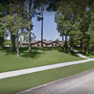 A suburban house surrounded by trees and a well-maintained lawn, with a sidewalk in the foreground.