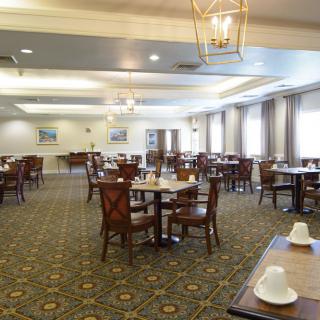 An empty dining room with neatly arranged tables and chairs, featuring elegant lighting and a carpeted floor.