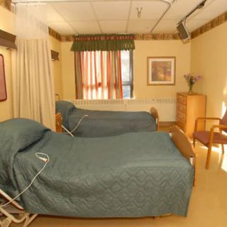 A hospital room with two adjustable beds and a window with curtains.