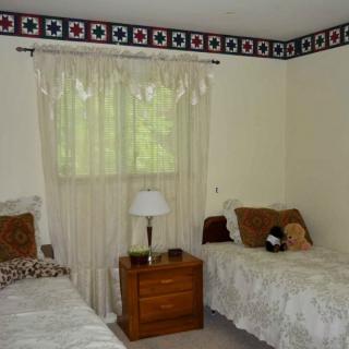 A cozy bedroom with two single beds, a nightstand, and a lamp by the window.