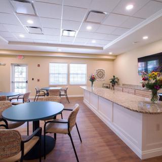 A well-lit dining area with tables, chairs, and a countertop, decorated with flowers.