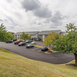 A suburban apartment complex with a large parking lot and surrounding greenery under a cloudy sky.