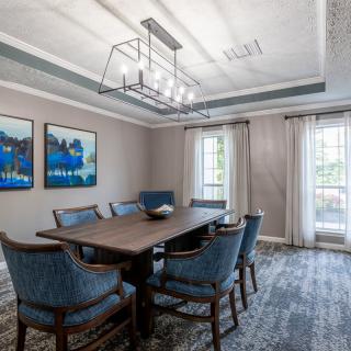 A beautifully designed dining room featuring a rectangular table surrounded by blue upholstered chairs, artwork on the walls, and a modern chandelier overhead.