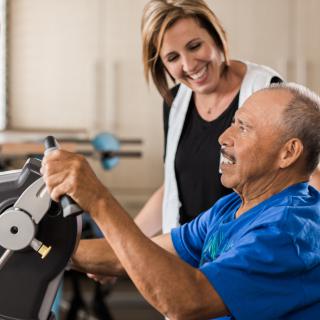 A healthcare professional assists an elderly man during a physical therapy session.