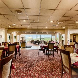 A spacious restaurant dining area with neatly arranged tables and chairs, featuring large windows in the background.