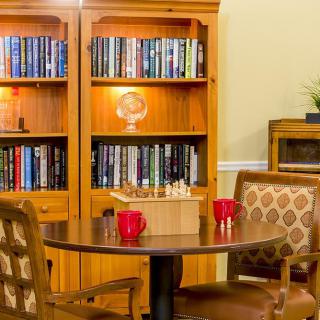 A cozy library setting with a wooden bookshelf, a round table, and chairs.