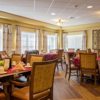 A cozy dining room with neatly arranged tables and chairs, featuring large windows and elegant decor.
