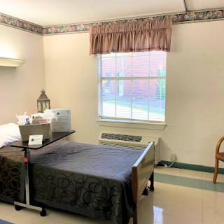 A view of a hospital patient room featuring two beds, basic furniture, and natural light coming through the window.