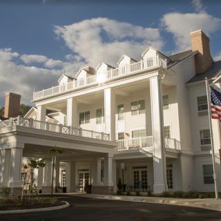 A grand white building with columns and an American flag, set against a partly cloudy sky.