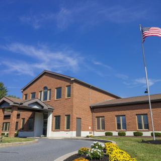 A brick building with an American flag and landscaped flowers under a clear blue sky.