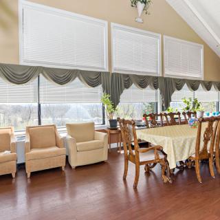 A spacious dining room with a long table, chairs, and large windows with curtains.