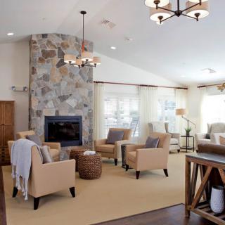 A cozy living room with modern amenities, featuring a stone fireplace and neutral-toned armchairs.