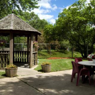 A serene garden setting featuring a wooden gazebo and outdoor furniture amidst lush greenery.