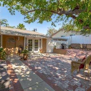 A sunny backyard with a spacious patio area, featuring outdoor seating and surrounded by trees.