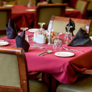 A neatly set dining table in a restaurant with red tablecloths and black napkins.