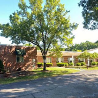 A serene view of a brick building surrounded by greenery on a sunny day.