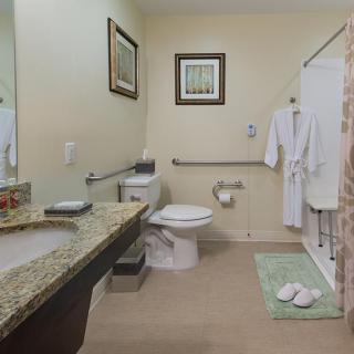A clean and well-decorated bathroom featuring a toilet, sink, and shower area with bathrobes and towels.