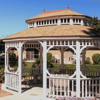 A charming white gazebo surrounded by green grass and blue skies.