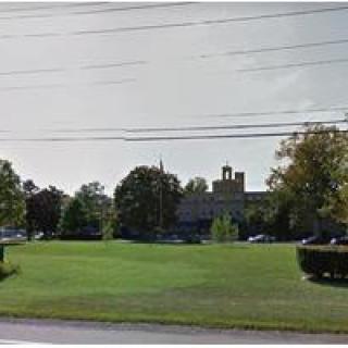 A church surrounded by trees and a large grassy area with power lines overhead.