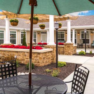 A peaceful outdoor patio area with tables, chairs, and a green umbrella set in a landscaped garden.