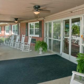 A cozy porch with white rocking chairs, potted plants, and glass doors.