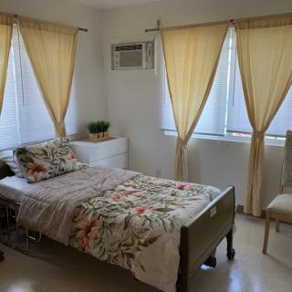 A cozy bedroom with a single bed, soft yellow curtains, and an air conditioner.