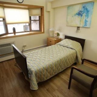 A cozy bedroom with a single bed, chair, and a large window allowing natural light.