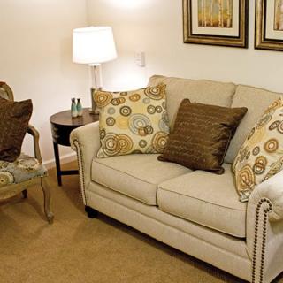 A cozy living room with a beige sofa, patterned throw pillows, and framed artwork on the wall.