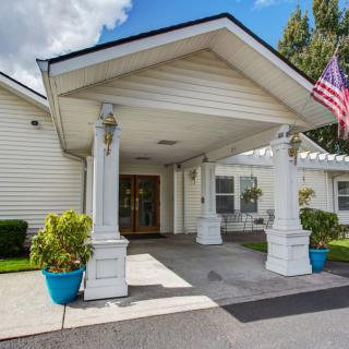A white building entrance with columns, featuring potted plants and an American flag.