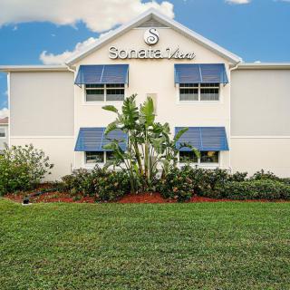 A well-maintained hotel building with a neatly landscaped lawn and blue awnings.
