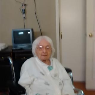 An elderly woman seated in a wheelchair inside a care facility.