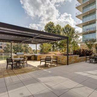 A modern outdoor patio with a pergola and seating area, set in an urban environment.