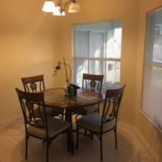 A cozy dining area with a round table and four chairs under a light fixture, next to large windows.