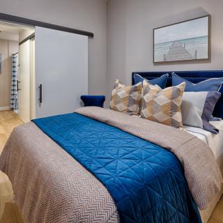 A modern bedroom featuring a neatly made bed with blue and beige accents, complemented by decorative pillows and a serene artwork on the wall.