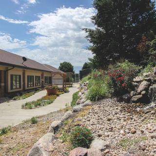 A building with a pathway surrounded by landscaped rocks and plants under a cloudy sky.
