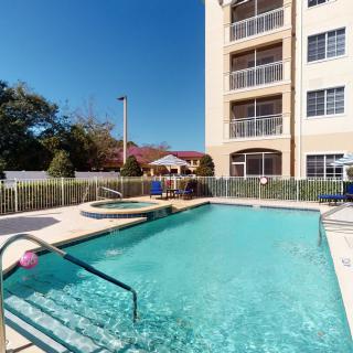 An outdoor swimming pool beside a multi-story apartment building on a sunny day.