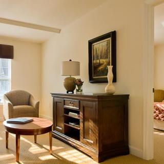 A cozy living room with a chair, round table, and a wooden cabinet adorned with a lamp and decorative items.