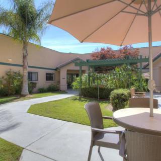 A tranquil patio area with chairs and an umbrella, surrounded by greenery and a building in the background.