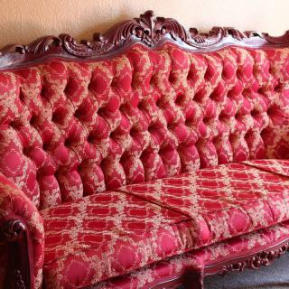 A vintage antique sofa with ornate wooden frame and red upholstered fabric.