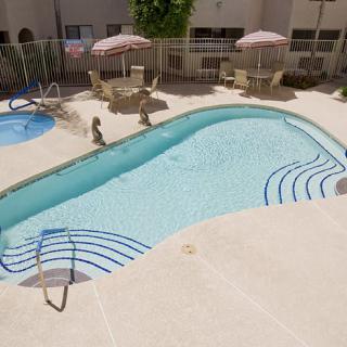 An outdoor swimming pool area with patio furniture and umbrellas on a sunny day.