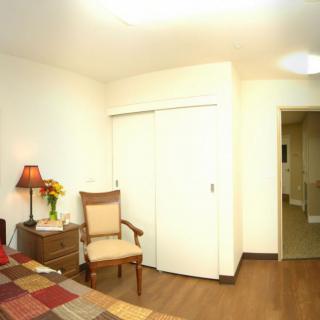 A cozy bedroom with a bed, chair, and lamp beside a closet.