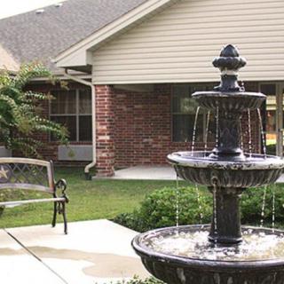 A tranquil garden scene featuring a multi-tiered fountain and a bench on a patio.