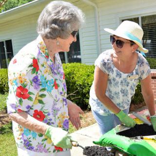 Two women engaging in gardening activities on a sunny day, showcasing teamwork and community spirit.
