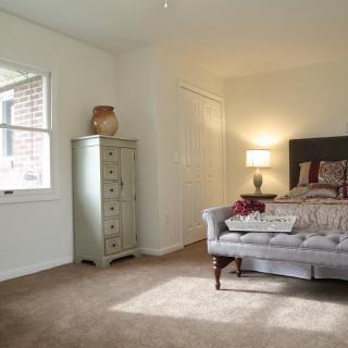 A cozy bedroom with a bed, sofa, cabinet, and a lamp, featuring neutral tones and natural light.
