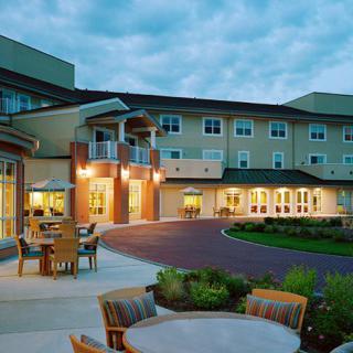 A well-lit retirement home with outdoor seating and landscaped surroundings at dusk.