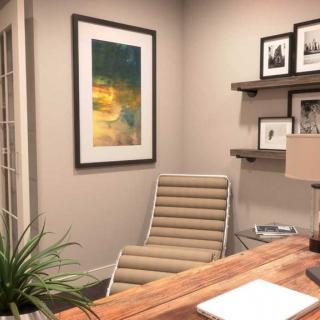 A cozy home office with a modern chair and wooden desk, featuring decorative artwork and shelves.