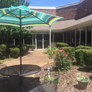 A sunny patio area with an umbrella and outdoor seating surrounded by a garden.