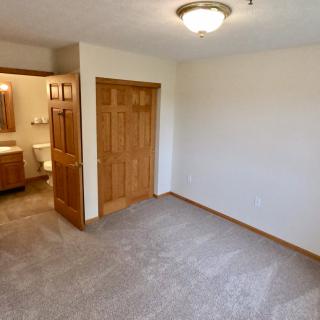 An empty carpeted bedroom with a wooden closet and an adjoining bathroom.