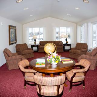 A spacious living room with a central table surrounded by chairs, featuring comfortable seating and decorative elements.