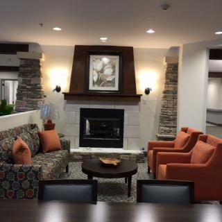 A cozy living room with a fireplace surrounded by a seating area, featuring a patterned couch and orange armchairs.